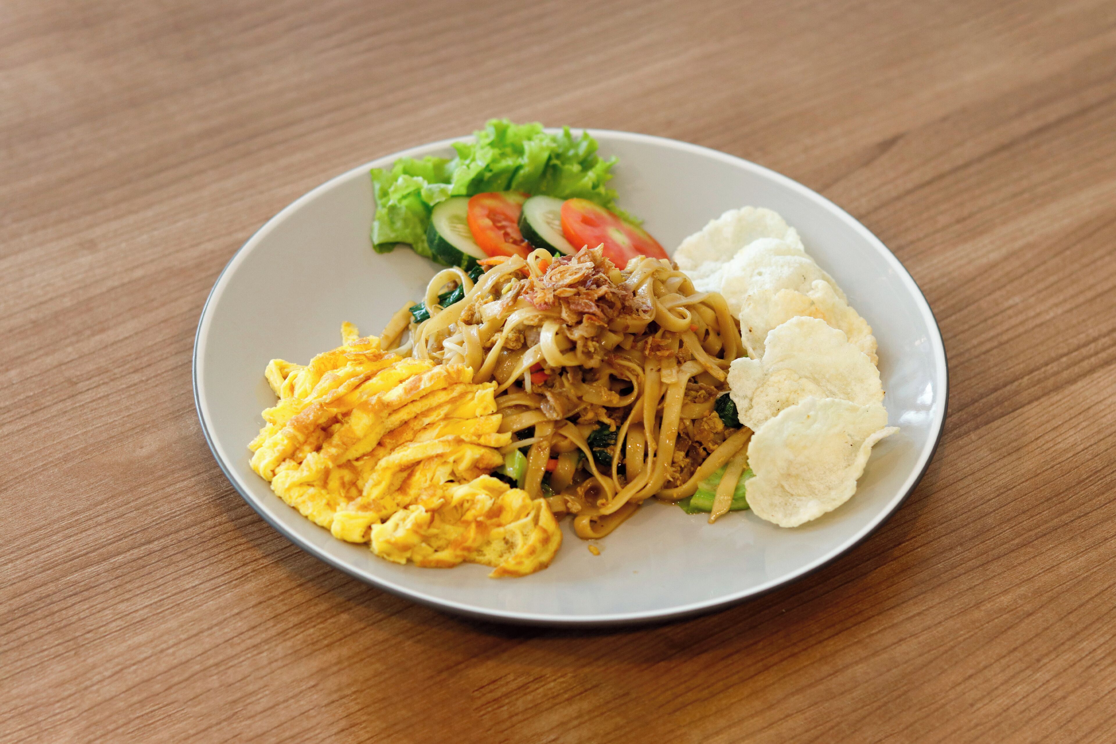 Un plato de comida con fideos, huevos revueltos y verduras.