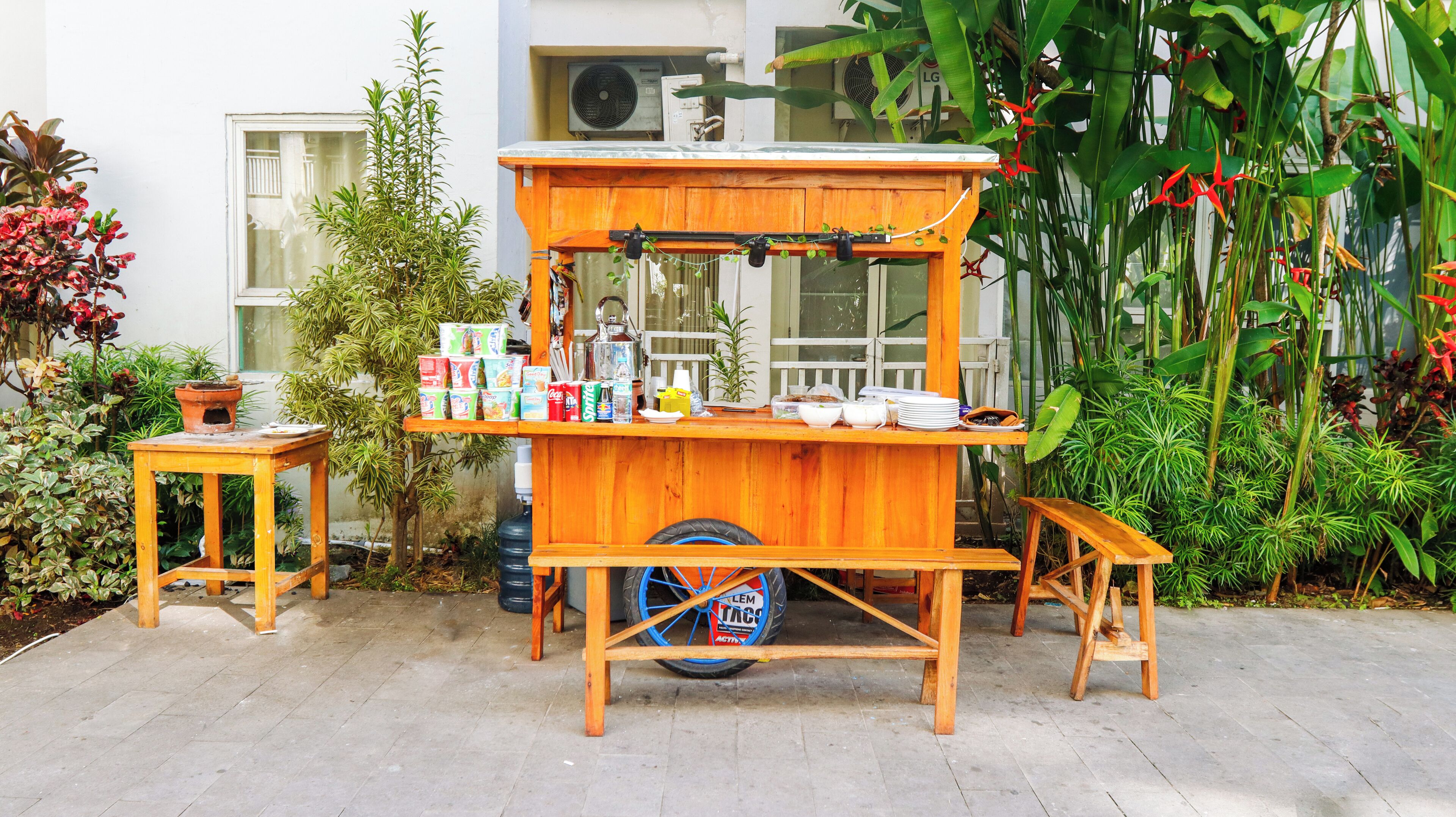 A wooden outdoor food cart with various food items and a bicycle wheel as a base.