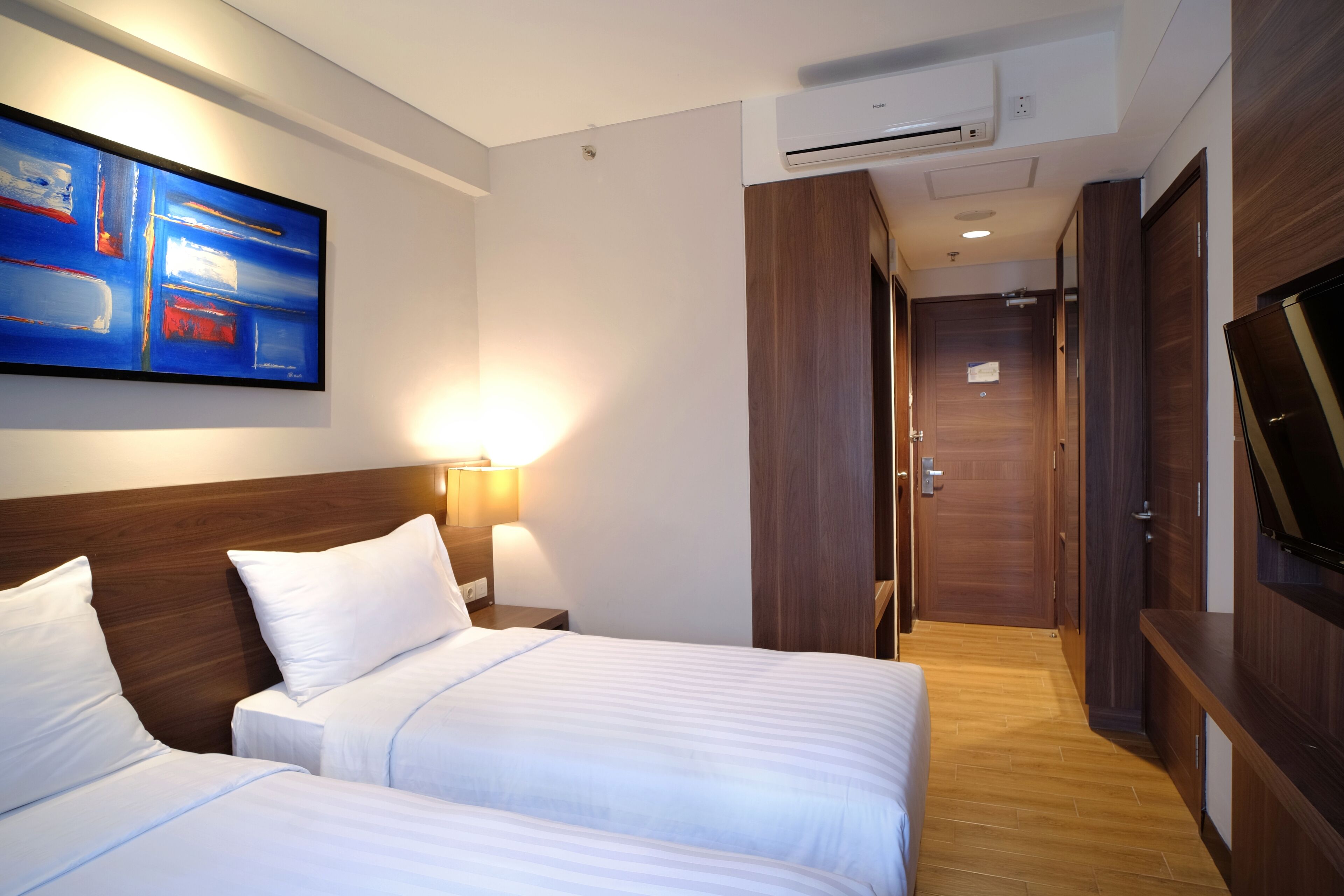 A hotel room with two beds, a painting on the wall, a TV, and a wooden wardrobe.