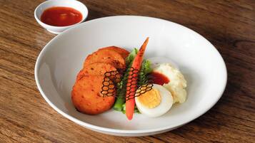 Un plato blanco con alimentos, incluyendo un huevo duro, puré de papas y frituras, acompañado de una pequeña cazuela de salsa.