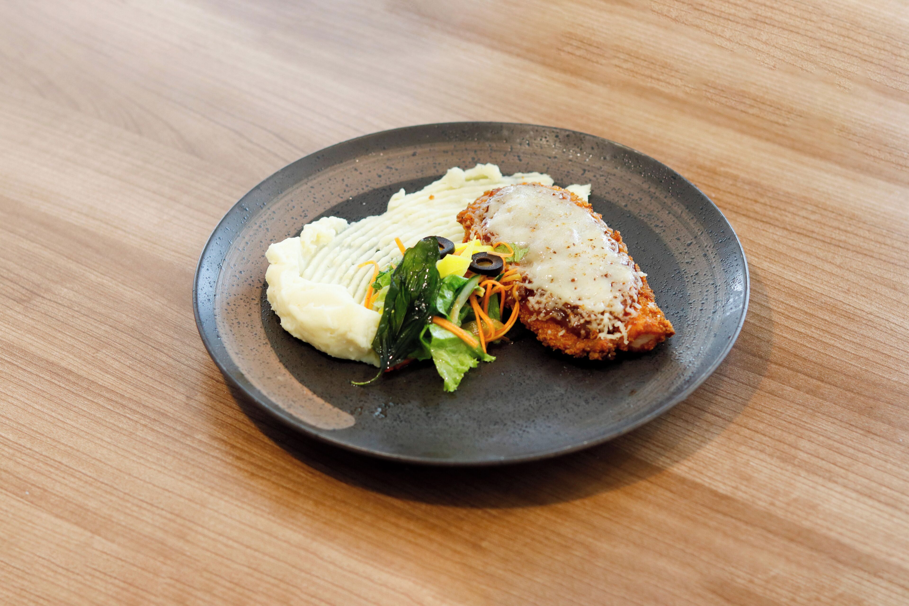 Un plato con puré de papas, un trozo de carne y una ensalada sobre una mesa de madera.