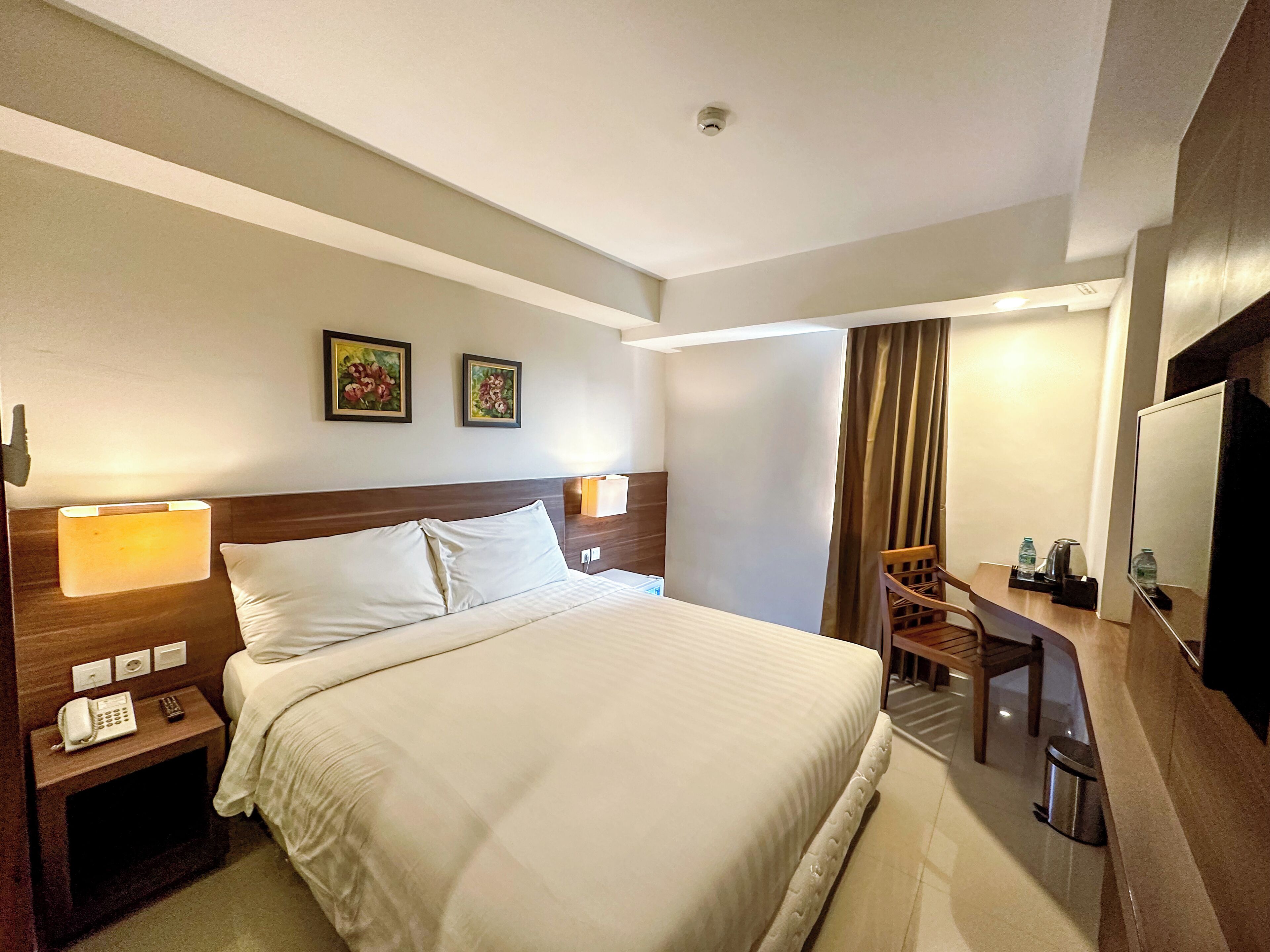Habitación de hotel con una cama grande, mesitas de noche con lámparas, un escritorio con silla y una televisión.