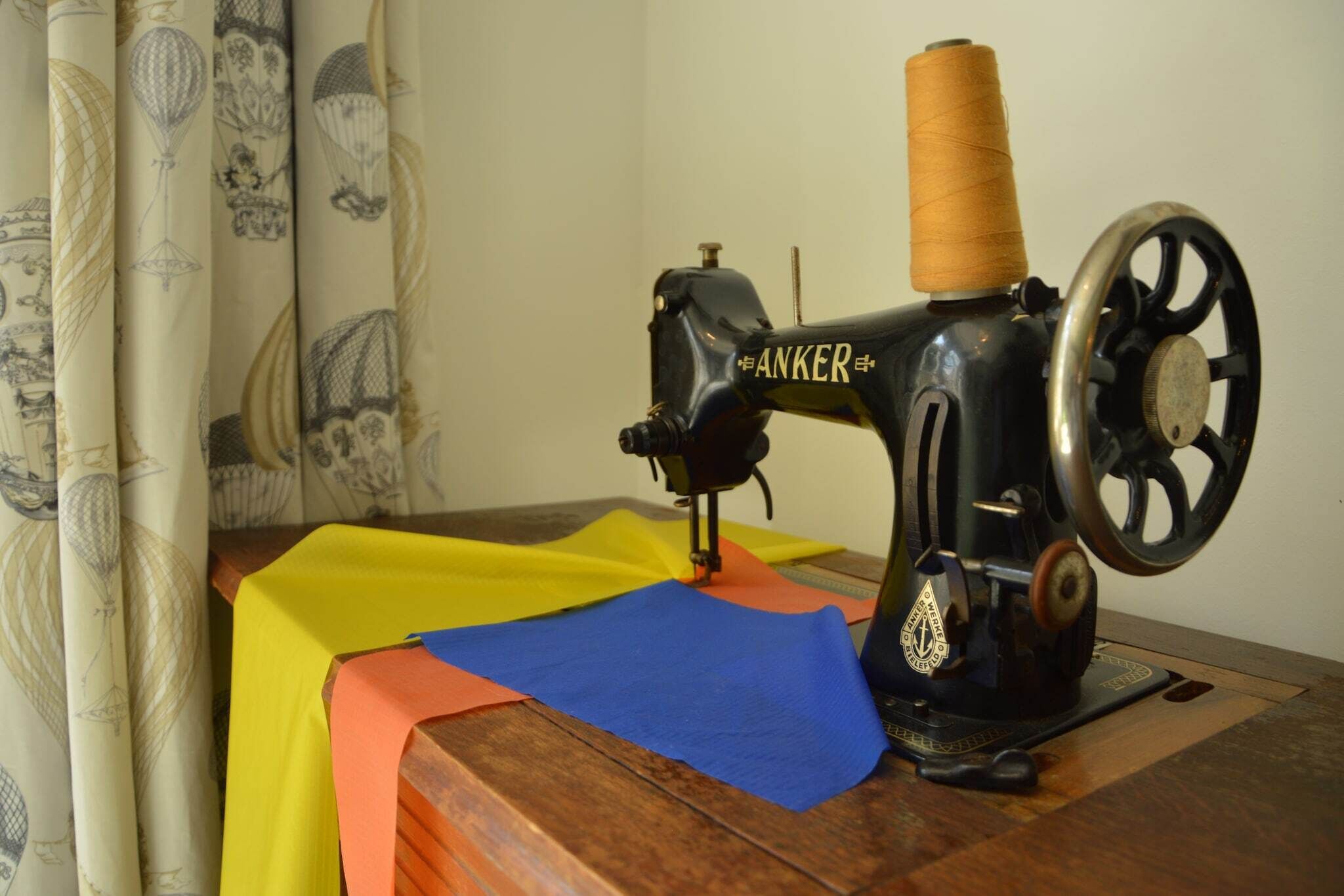 A vintage Anker sewing machine with a spool of thread on a wooden table.