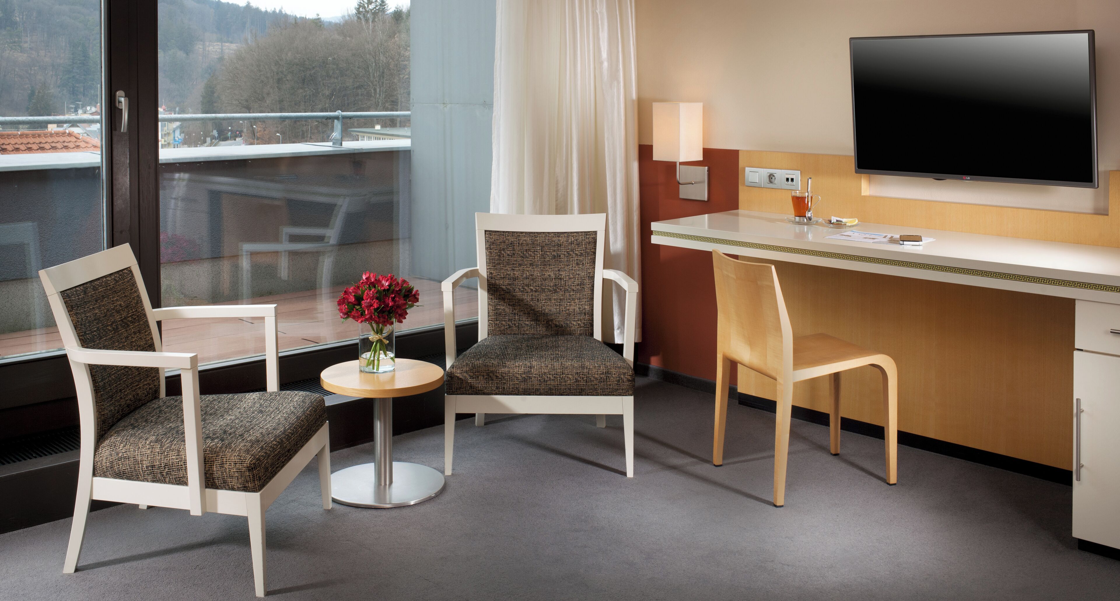 Une chambre d’hôtel équipée d’un bureau, de deux chaises, d’une télévision et d’une fenêtre donnant sur un pont et des arbres.