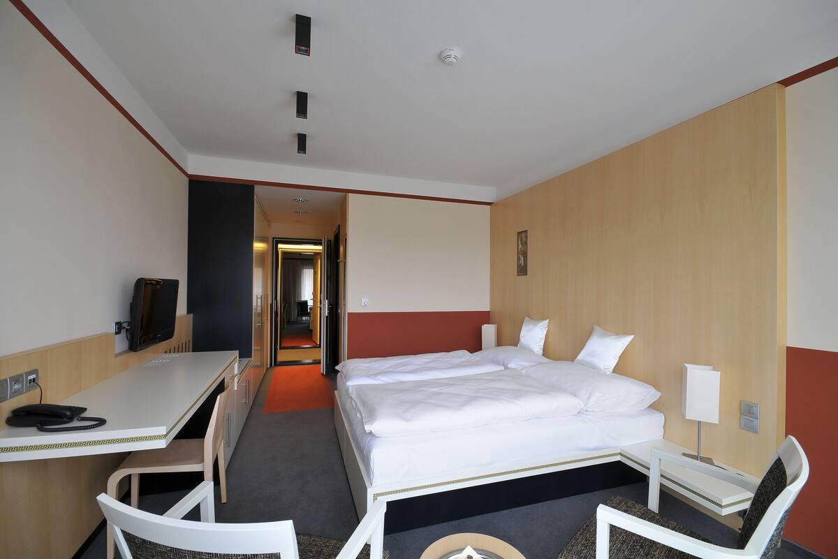 A hotel room with a bed, a desk, a chair, a TV, and a door leading to another room.