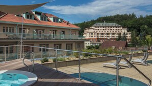 Un espace piscine sur le toit, avec des bains à remous, une terrasse en bois et une vue sur les bâtiments de l’hôtel.
