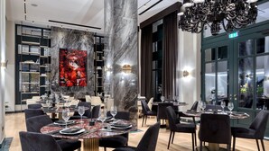 A modern dining area with marble columns, black upholstered chairs, and a large painting on the wall. - Grand Hotel Kalamata (Kalamata)