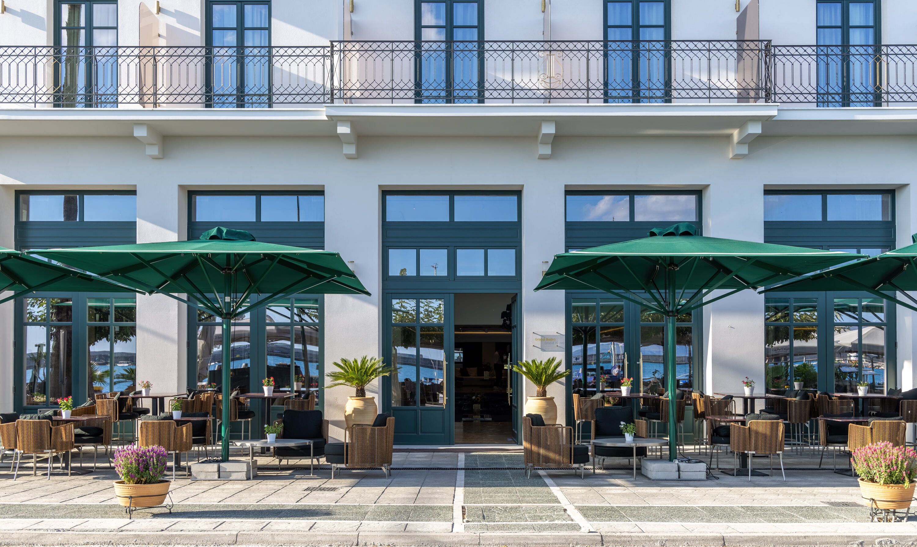 Ein Hotel mit doppeltem Eingang, Außenbereich mit grünen Sonnenschirmen und Blick auf das Meer.