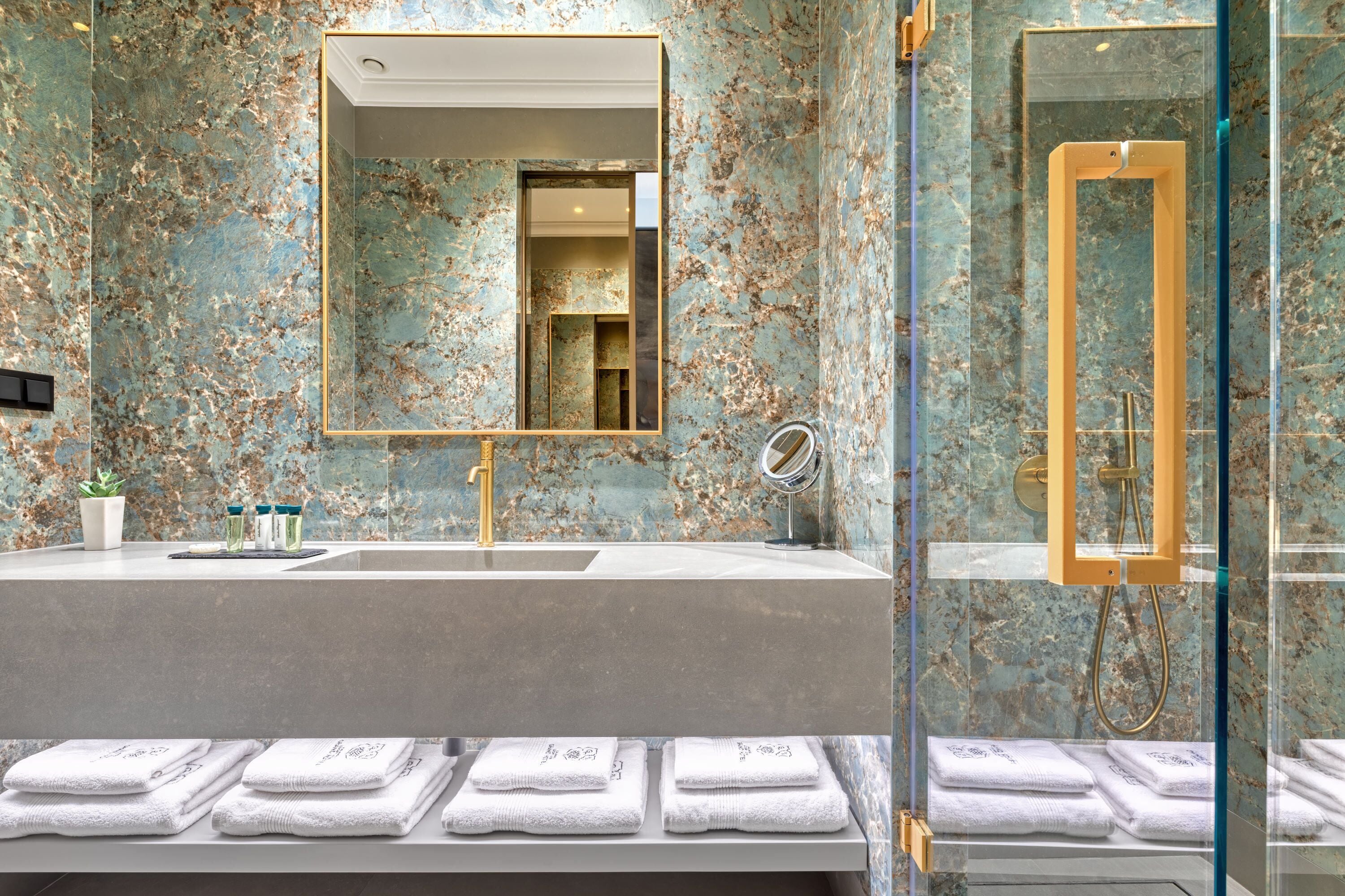 Une salle de bain avec un mur en marbre, deux lavabos, un grand miroir et une douche en verre.