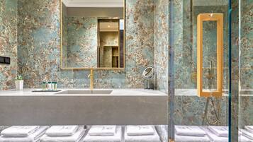 Une salle de bain avec un mur en marbre, deux lavabos, un grand miroir et une douche en verre.