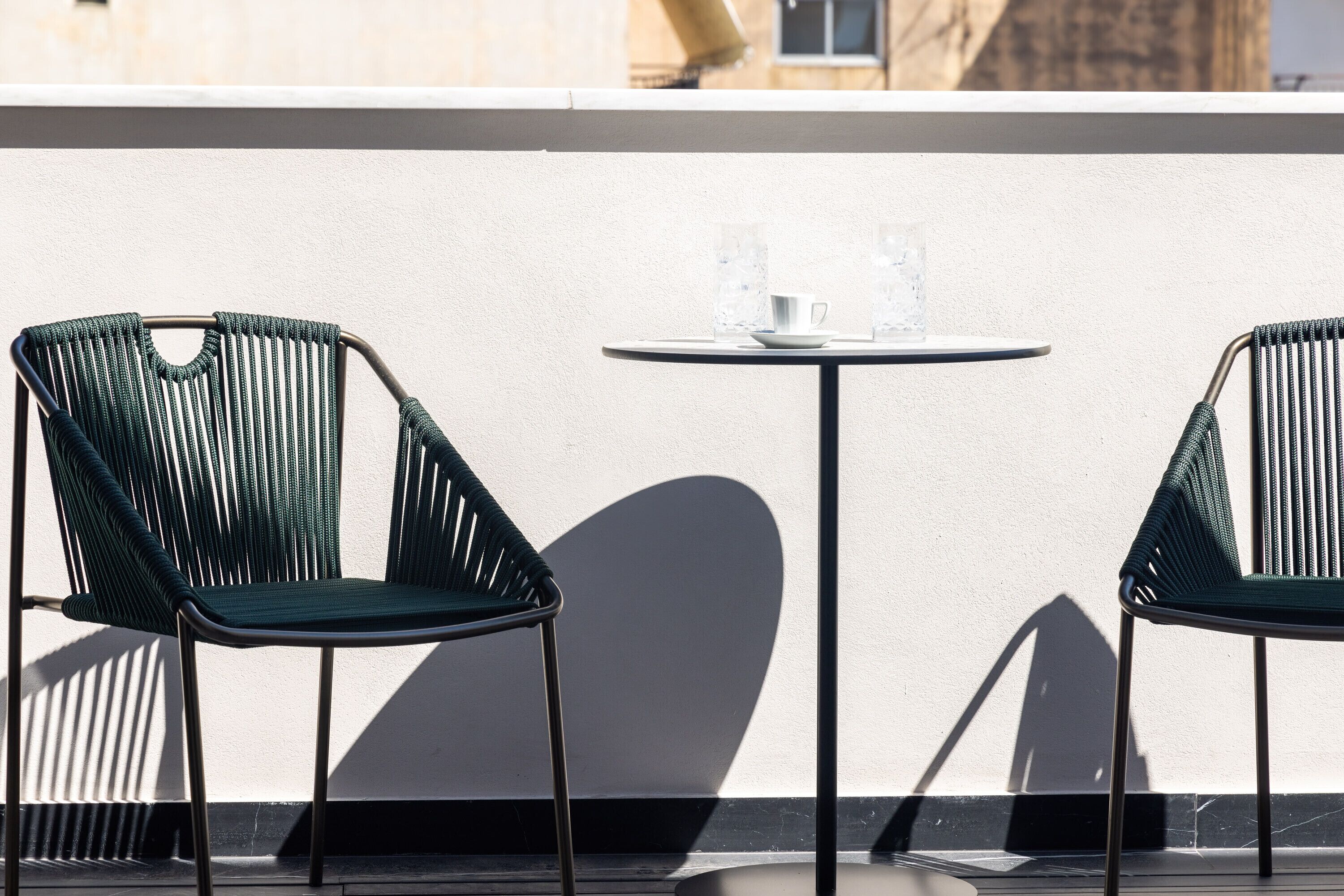 Two green chairs and a small round table with two glasses of water on a balcony.