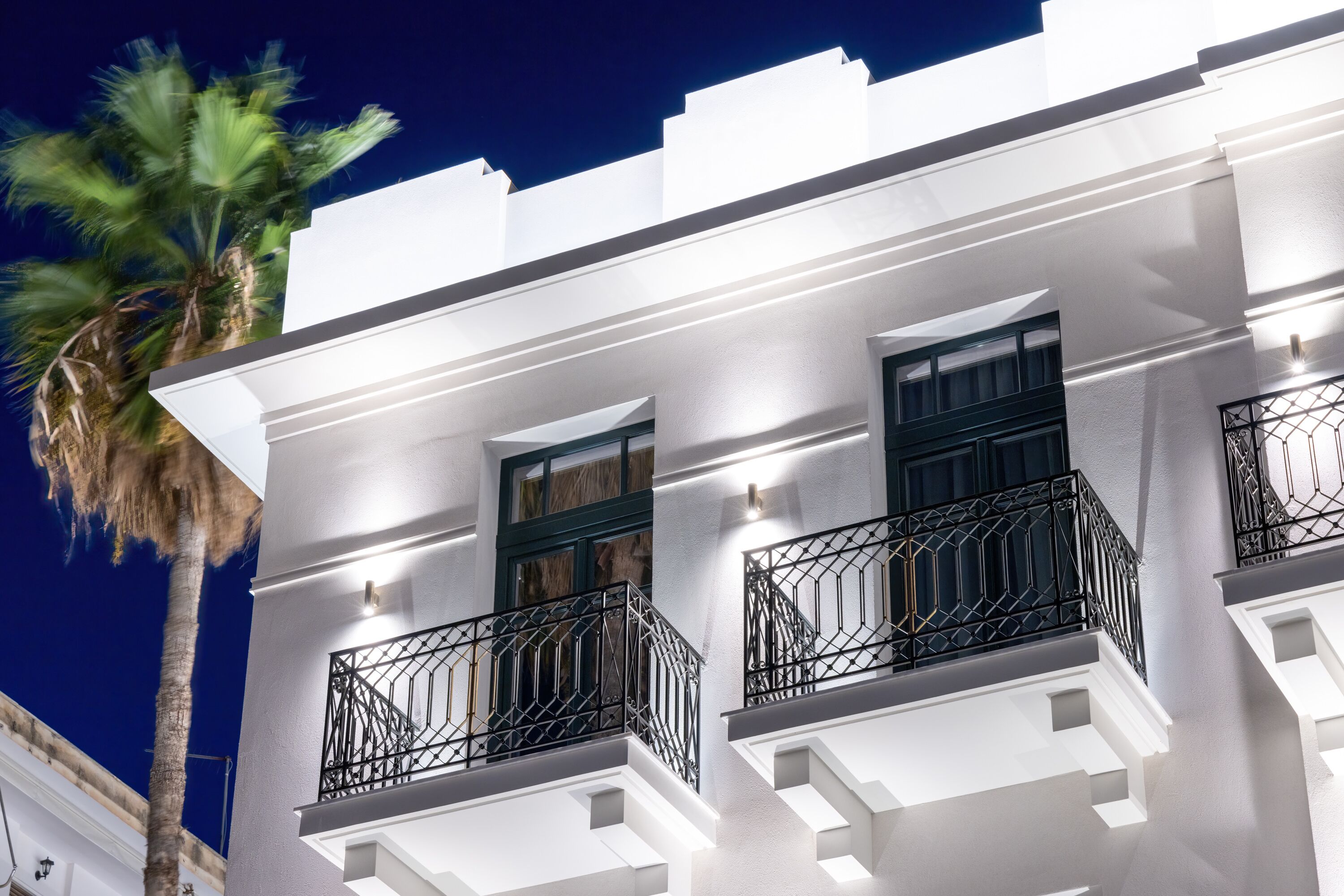 A white building with balconies and a palm tree.