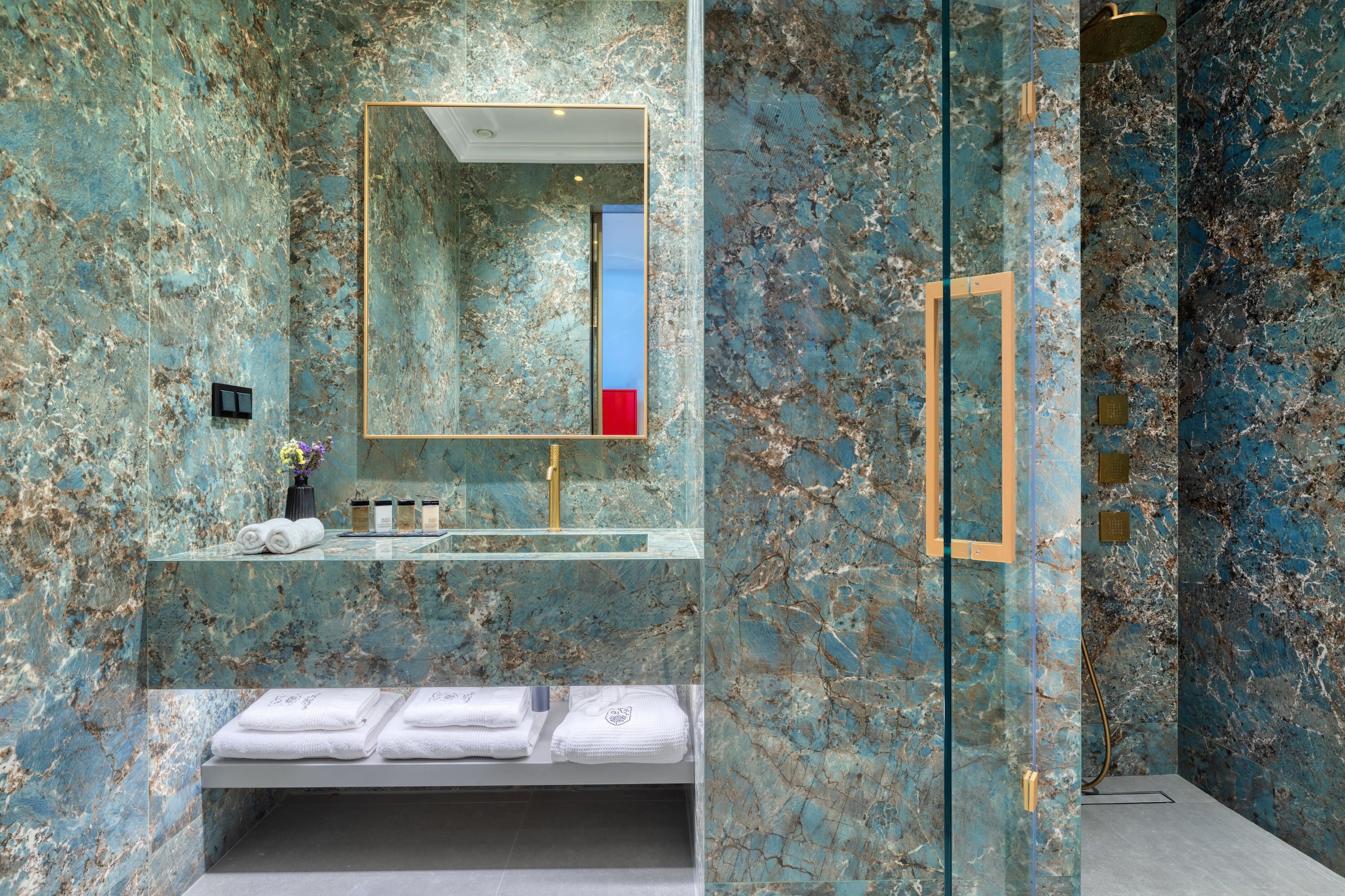 A bathroom with a marble wall, a sink, a mirror, and a shower area.