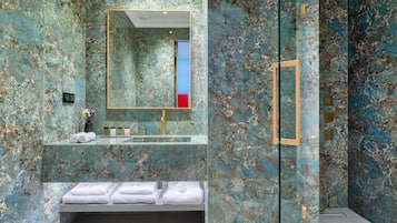 A bathroom with a marble wall, a sink, a mirror, and a shower area.