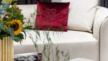 A white sofa with a red cushion featuring a crest, a vase with sunflowers, and a black and white patterned pillow.
