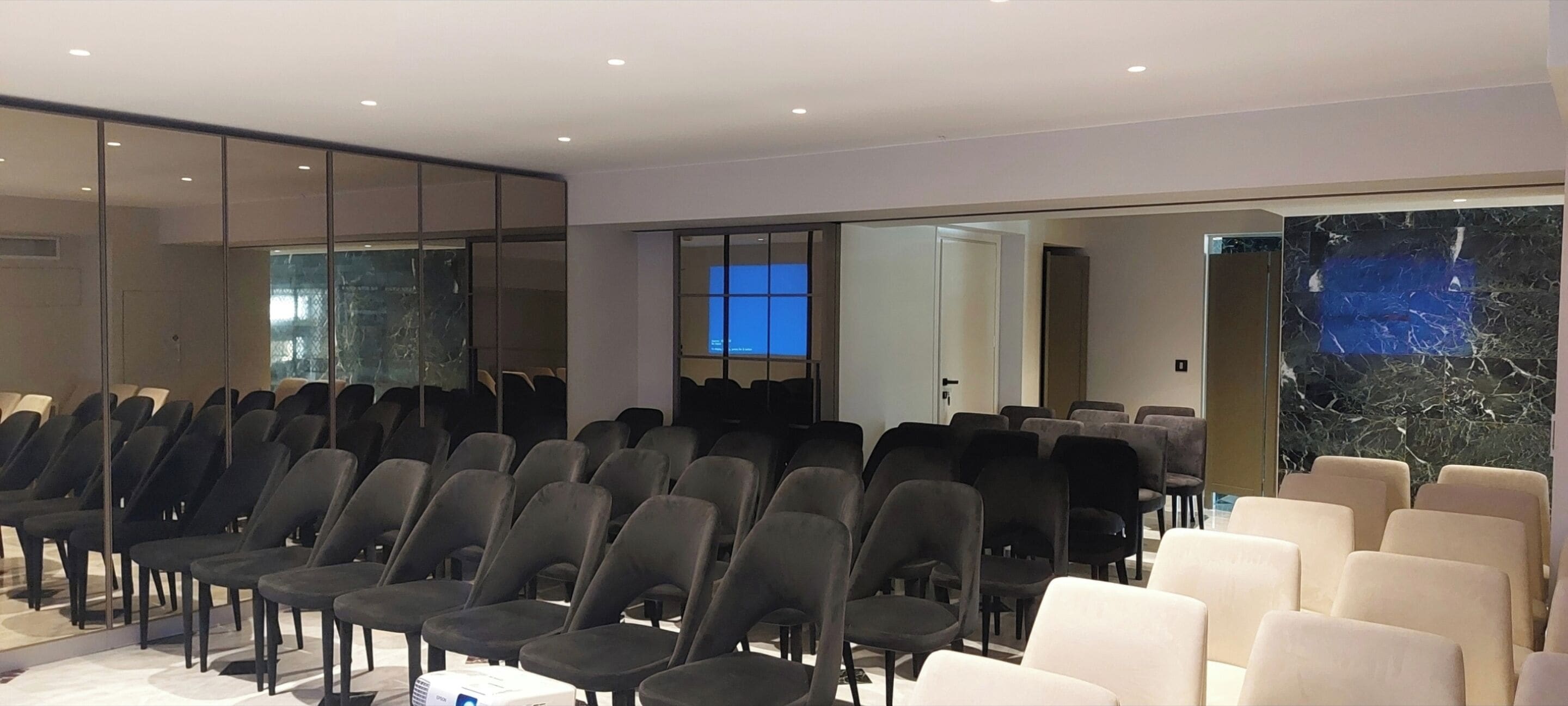 A conference room with rows of chairs, a large mirror, and a marble wall.