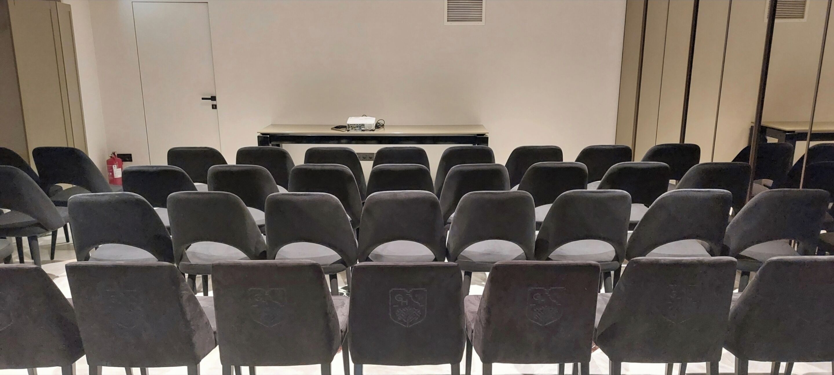 A conference room with rows of chairs facing a table with a projector.