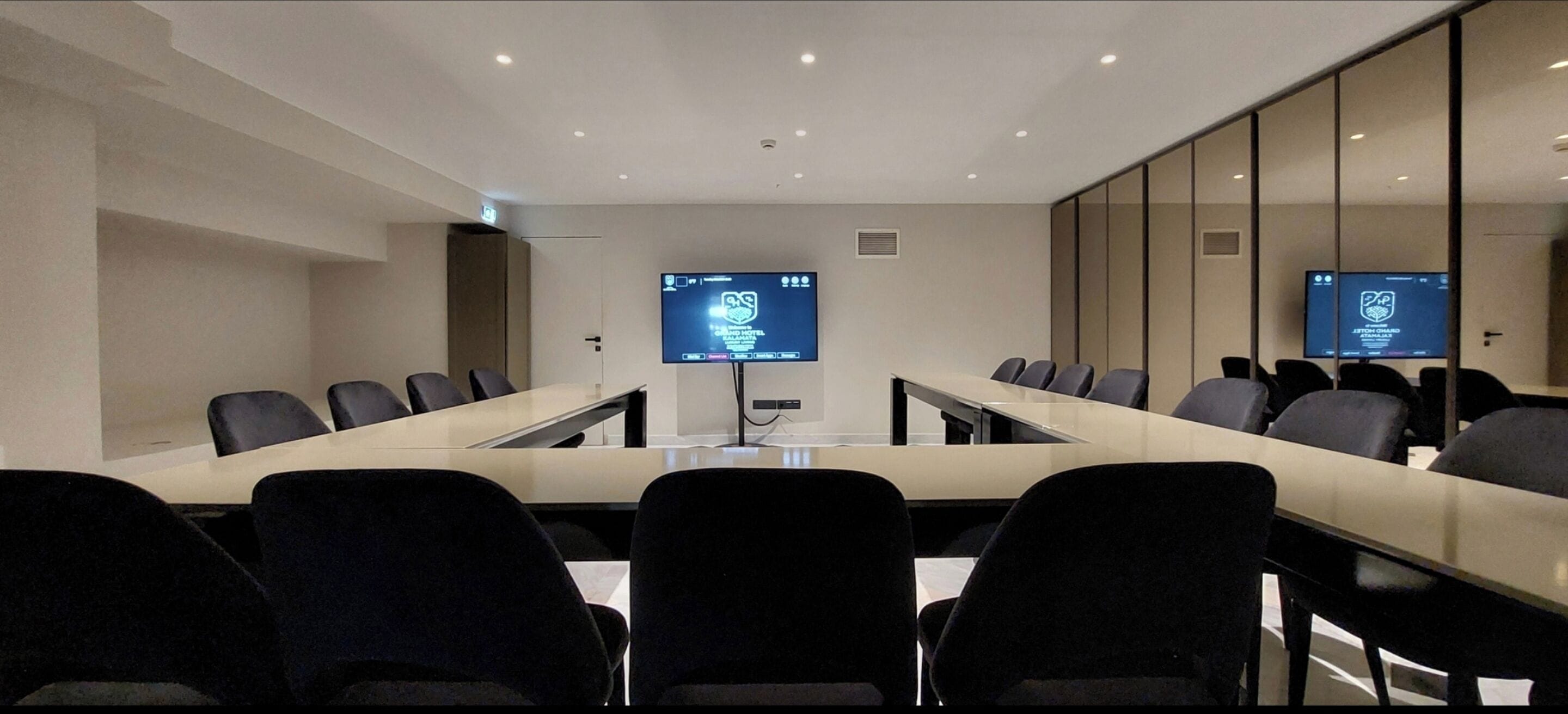 A conference room with a long table, multiple chairs, and two screens displaying content.