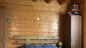 Een houten kamer met een bed, een kledingkast en een klein tafeltje met een lamp.