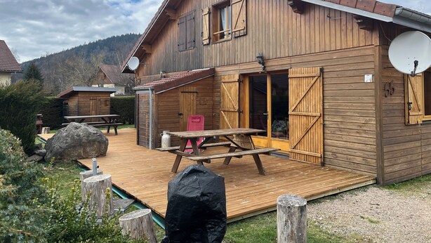 Een houten chalet met een terras, een schotelantenne en een grote rots op de voorgrond.