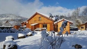 Een houten hut met een sneeuwbedekte dak, omringd door besneeuwde grond en bomen.