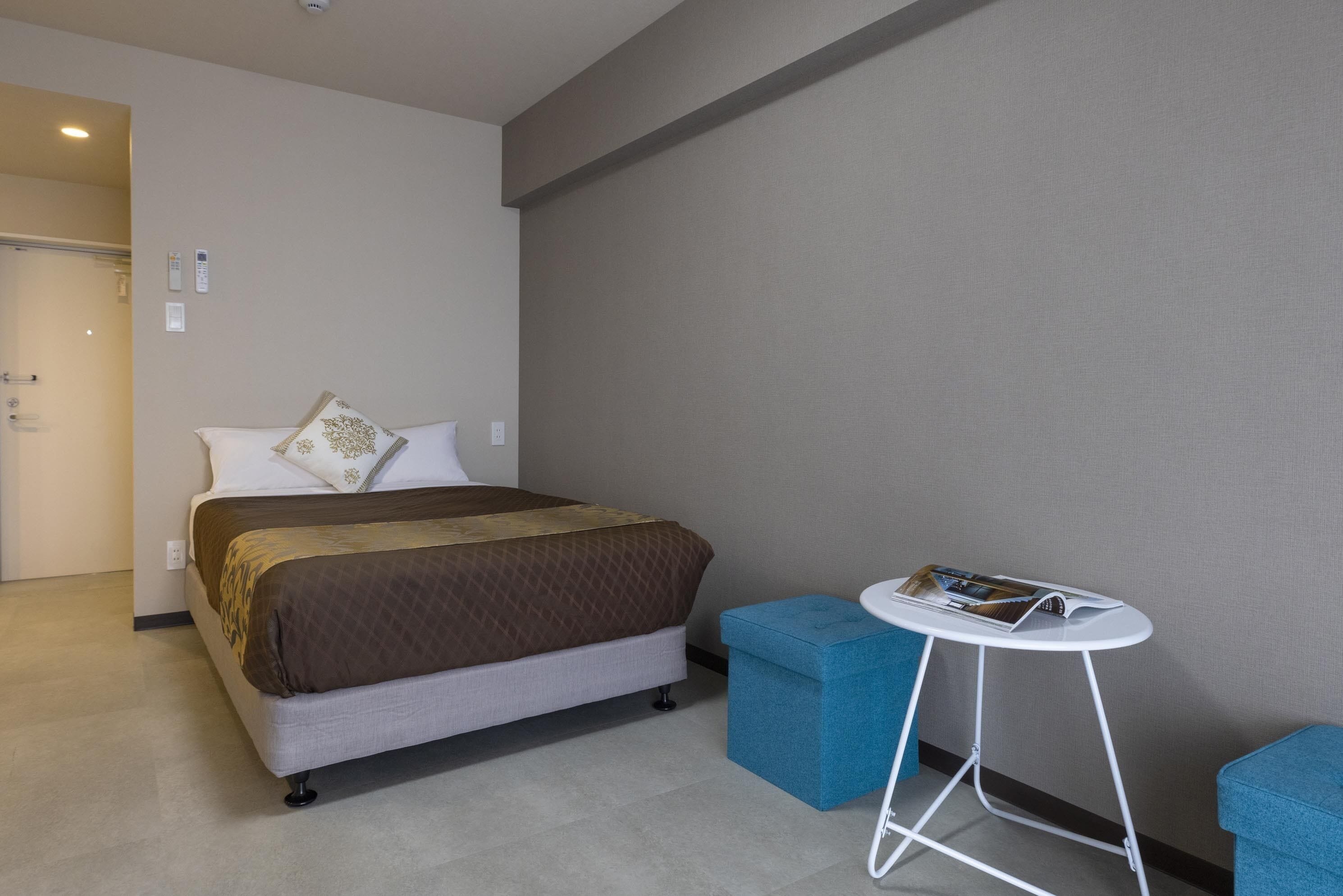 A hotel room with a bed, a small table, and a blue chair.