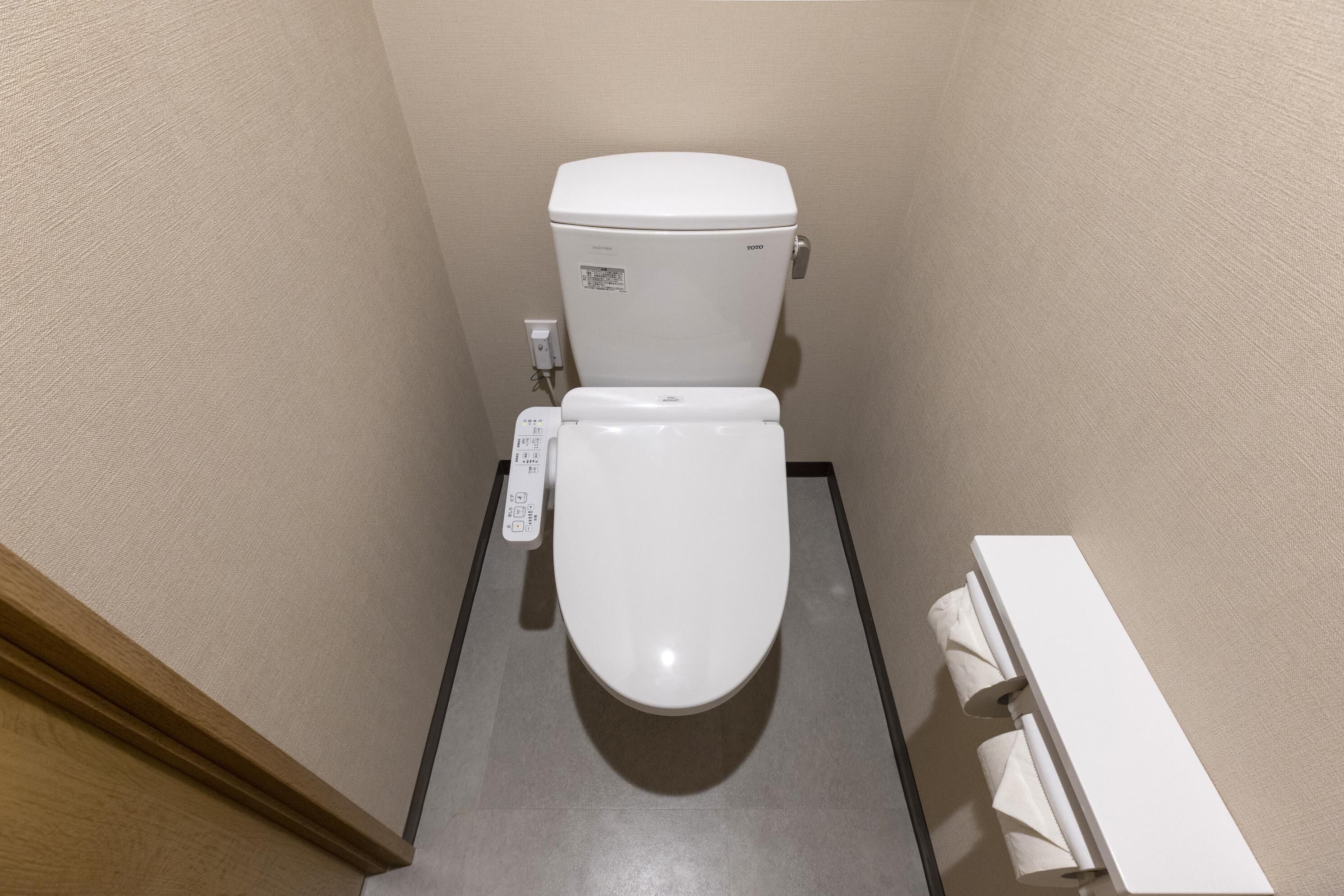 Un baño pequeño y moderno con inodoro, secamanos integrado en la pared y un perchero para toallas.