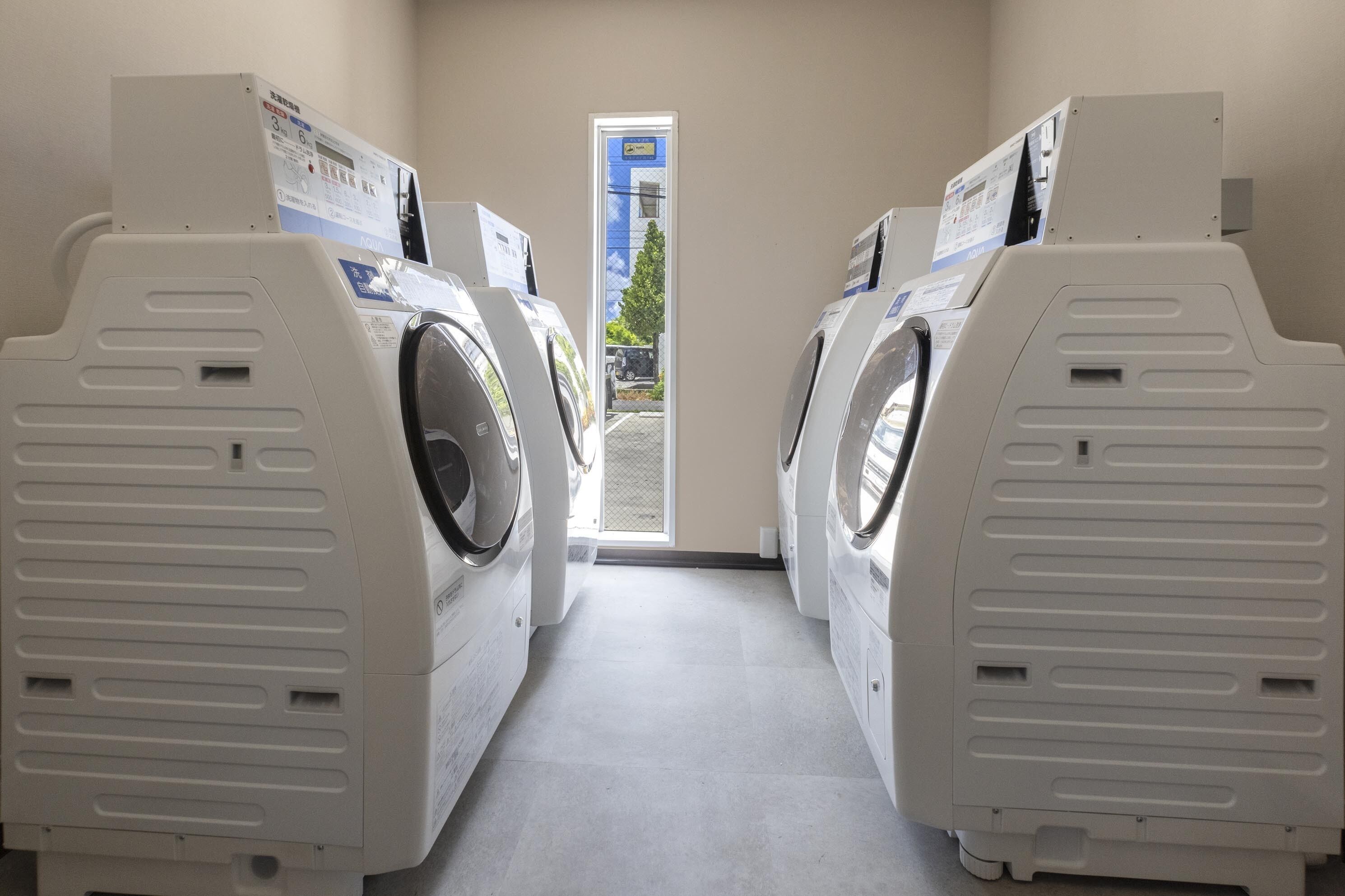 A laundry facility with multiple washing machines and dryers, a tiled floor, and a door leading outside.