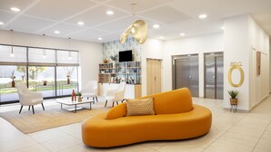 A modern lobby with a curved orange sofa, white chairs, a coffee table, and a bookshelf. - Residhome Nice Aéroport (Nice)