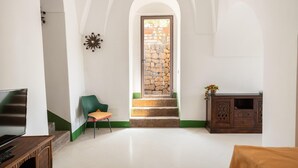 Una habitació àmplia amb una escala que condueix a una paret de pedra, una cadira verda, un armari de fusta i un televisor sobre un moble de fusta.