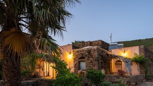 Edifici de pedra amb teulada de palla, envoltat de vegetació exuberant i una palmera.