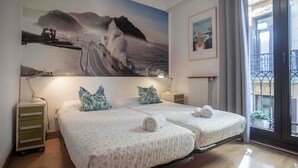 A double bed room with a large ocean wave painting on the wall, a small desk with a lamp, and a balcony with a railing. - Pensión Gurtxu by Sun Sebastián (San Sebastián)