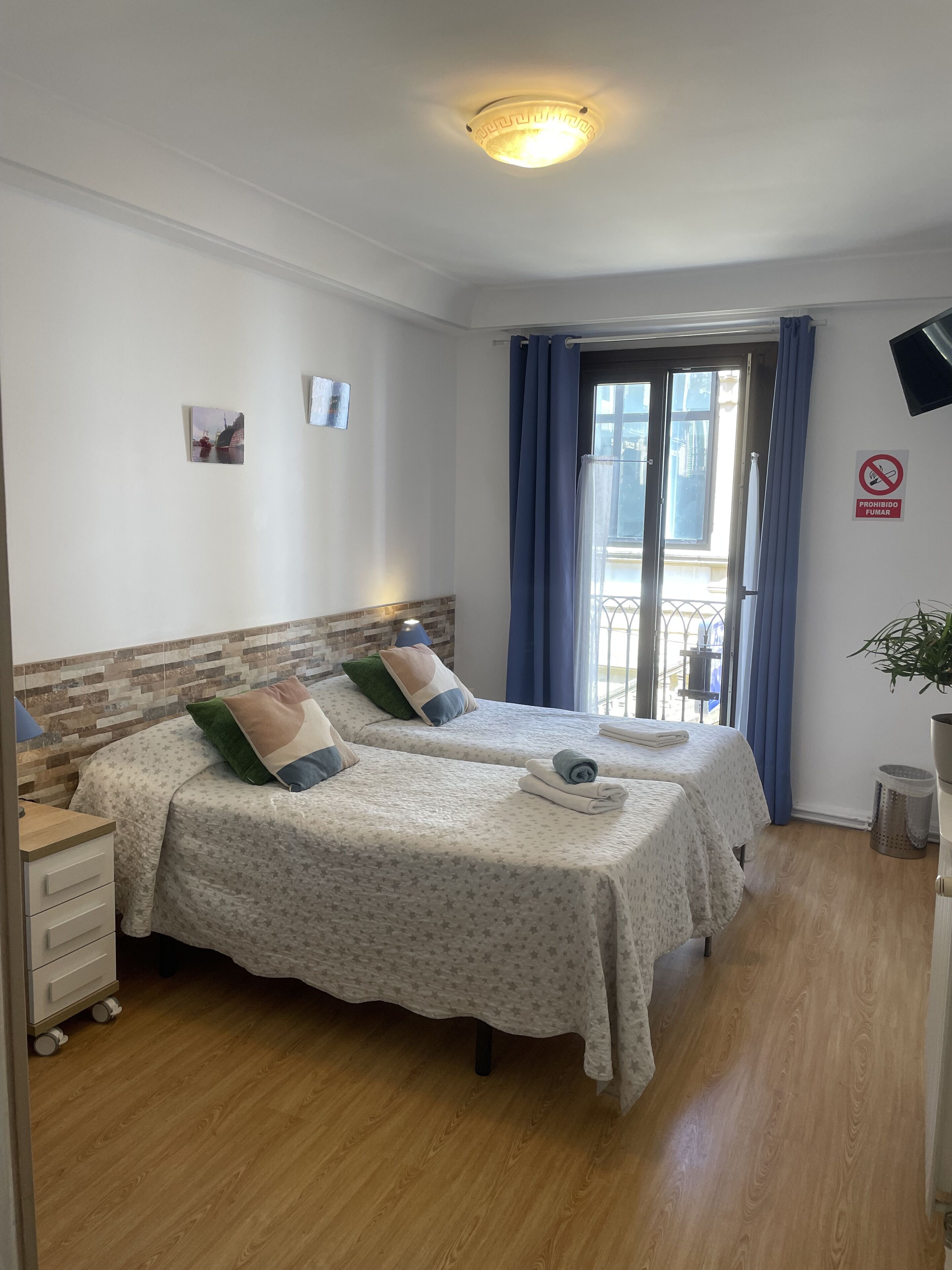 Quarto de hotel com duas camas, uma escrivaninha pequena, uma lixeira e vista para a varanda.
