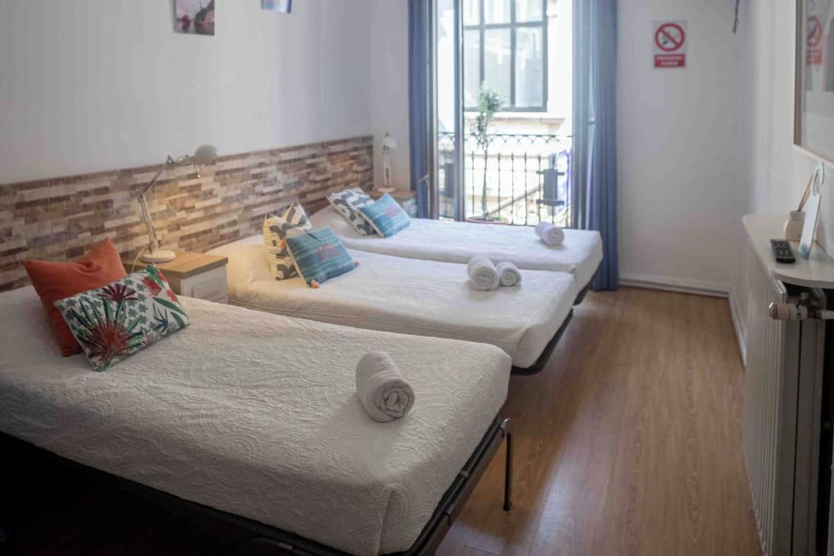 Habitación de hotel con dos camas, ventilador de techo, ventana con vistas, televisión y radiador.