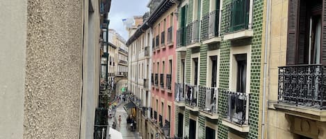 A narrow street with multi-story buildings, balconies, and outdoor seating areas.