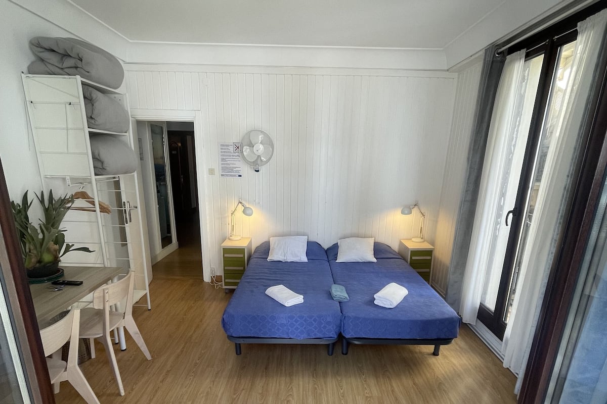 Habitación con dos camas, un escritorio y una silla. Cuenta con ventilador de techo y ventana con cortinas.