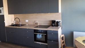 A modern kitchen with dark cabinets, a wooden countertop, a sink, a coffee maker, and an oven.