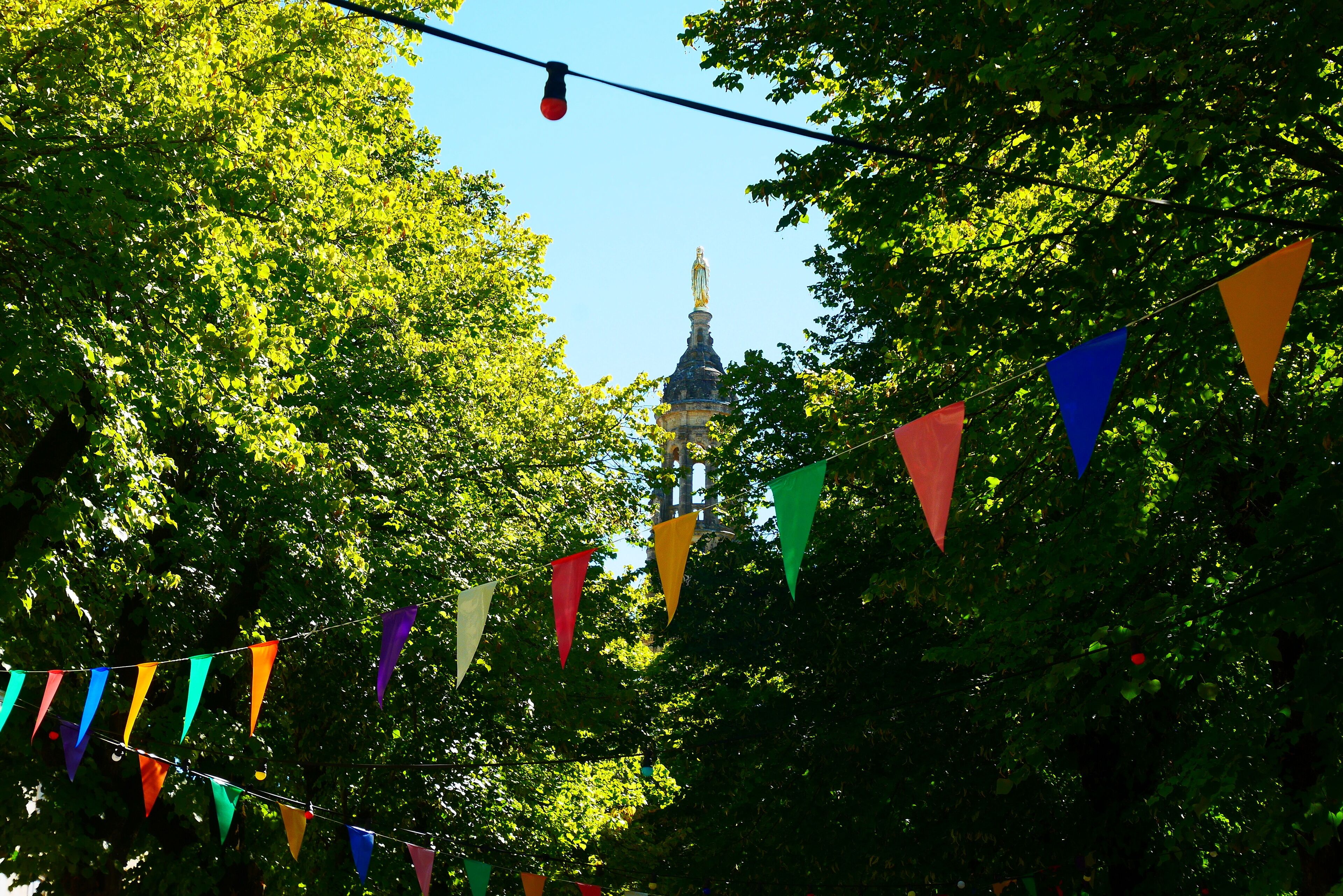 A view of a building with a statue on top, surrounded by trees and colorful triangular flags.