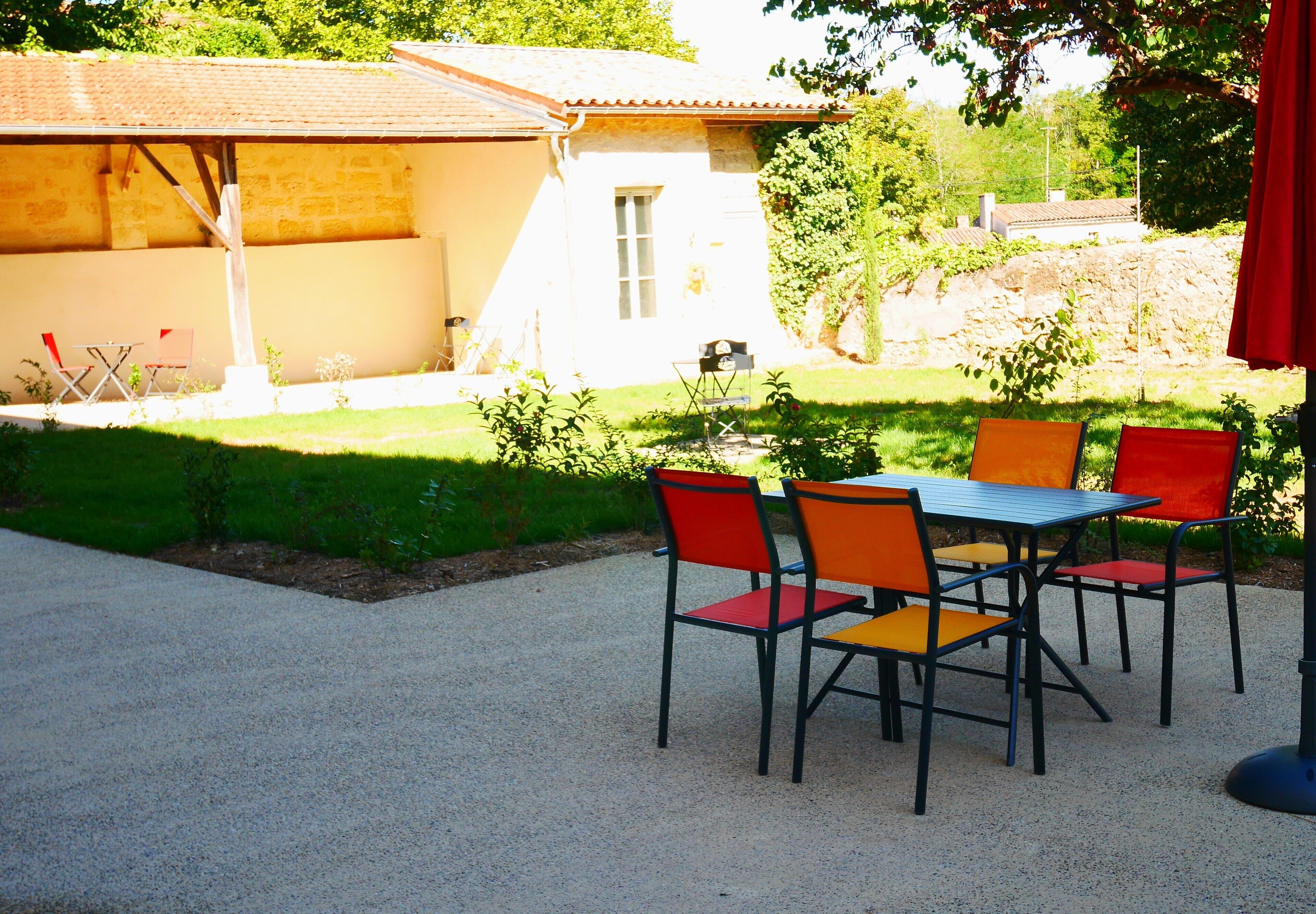 Een terras buiten met een tafel en stoelen, een overdekt zitgedeelte en een gebouw op de achtergrond.