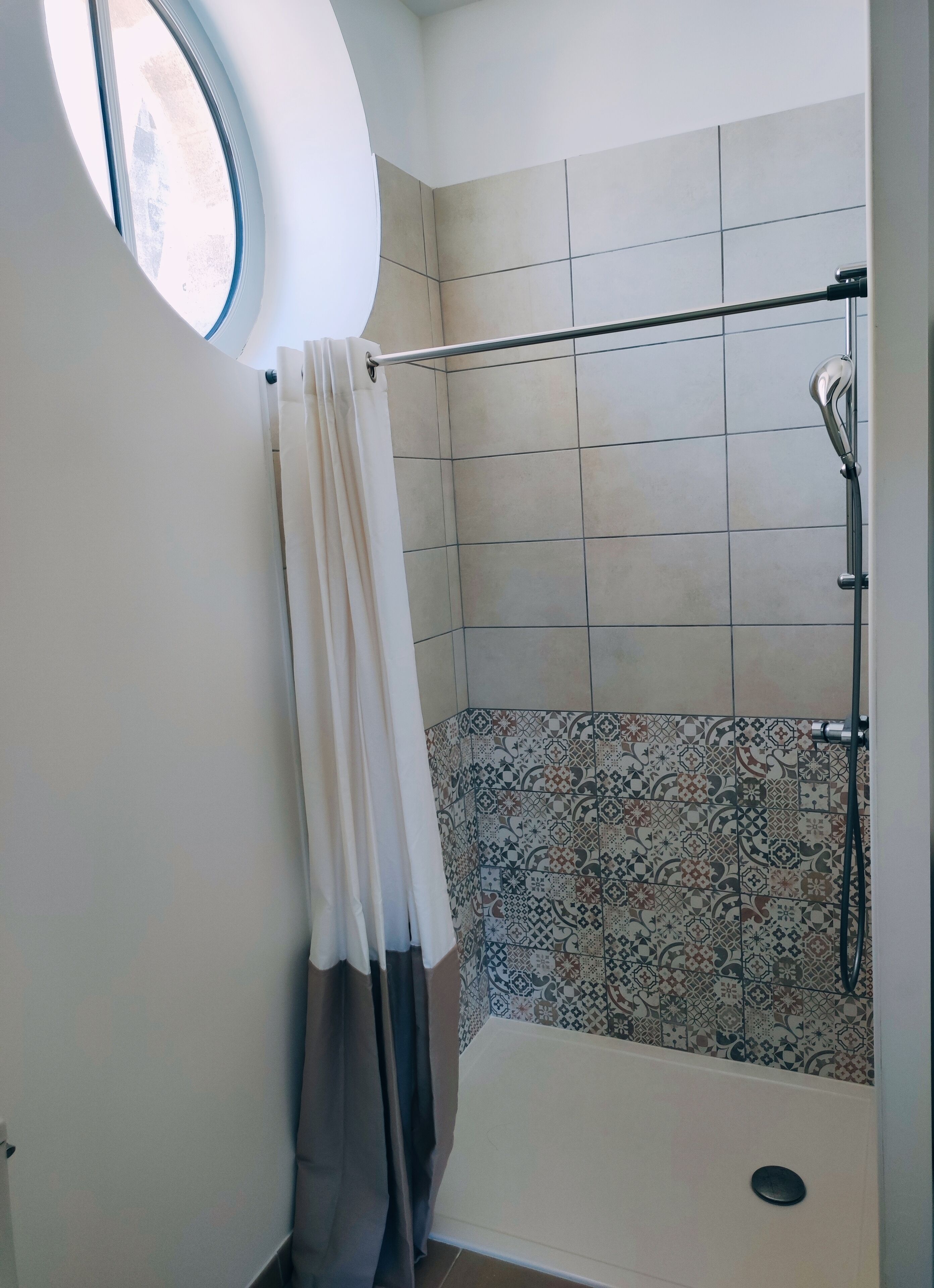 Douchegedeelte met betegelde wand, douchekop en douchegordijn.