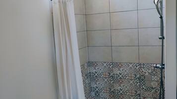 Douchegedeelte met betegelde wand, douchekop en douchegordijn.