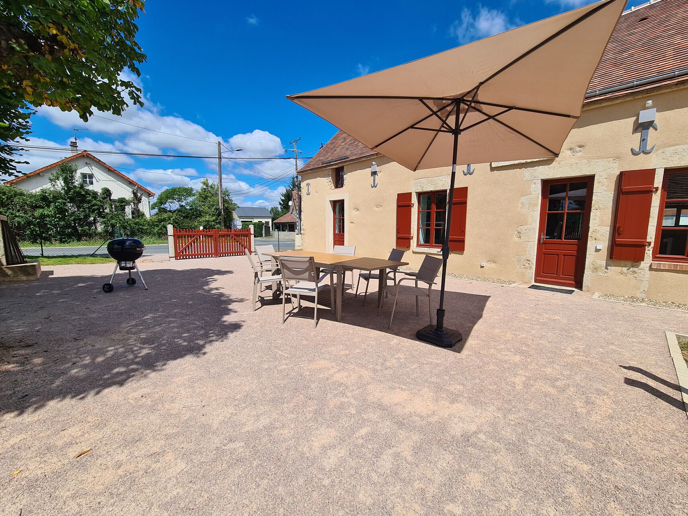 Un patio con tavolo e sedie, un barbecue e un ampio ombrellone.