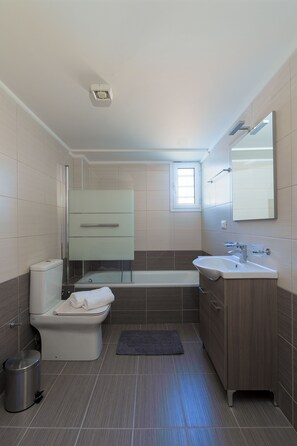 A modern bathroom with a toilet, bathtub, and sink. - Oikies. Luxury Apartment with Old Mill View | private free parking area  (Agios Nikolaos)