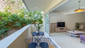 Ein modernes Wohnzimmer mit Flachbildfernseher, Couchtisch und Sofa. Es gibt einen Balkon mit Tisch und Stühlen sowie einen Blumentopf.