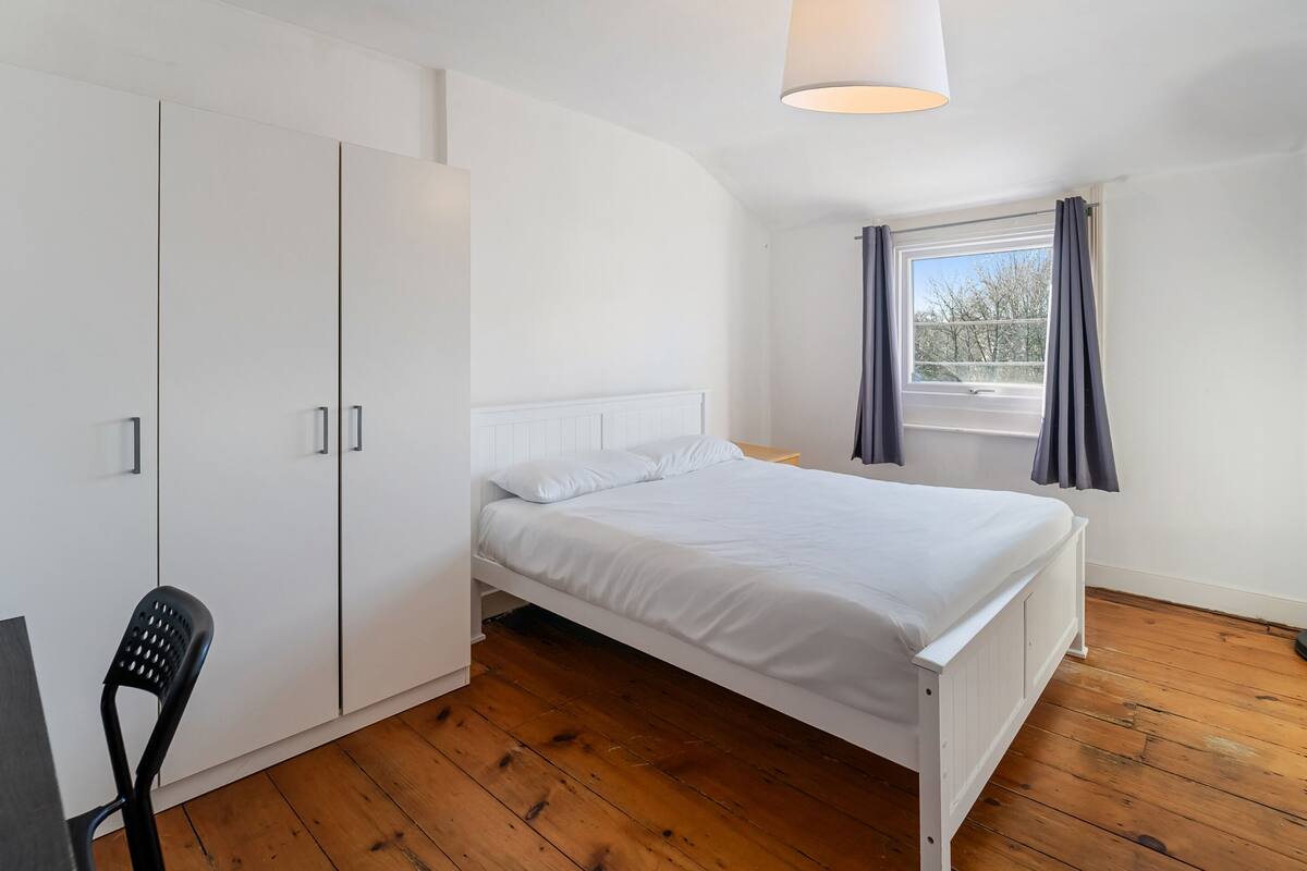 Une chambre à coucher avec un lit, une armoire blanche et une fenêtre avec des rideaux.