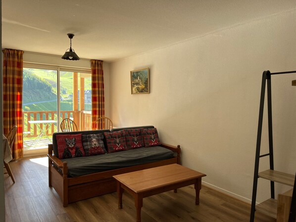 A cozy room with a wooden sofa, a small table, and a view of a green landscape through large windows.