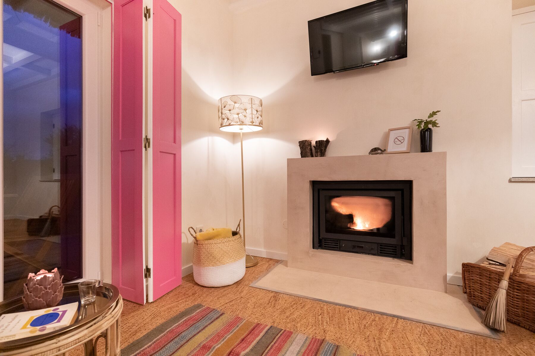 A living room with a fireplace, a pink door, a flat-screen TV, and a floor lamp.