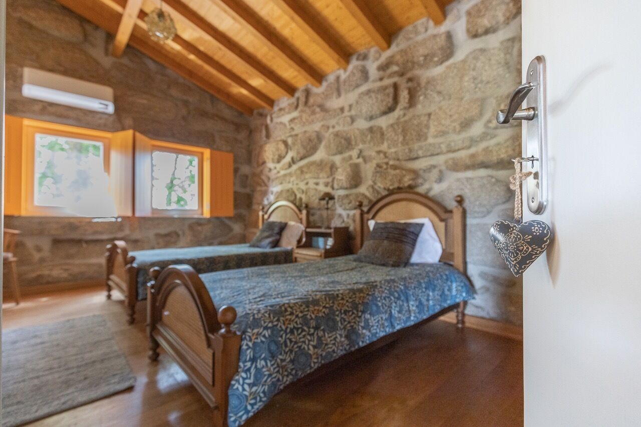 A rustic room with two wooden beds, a stone wall, and a wooden ceiling.