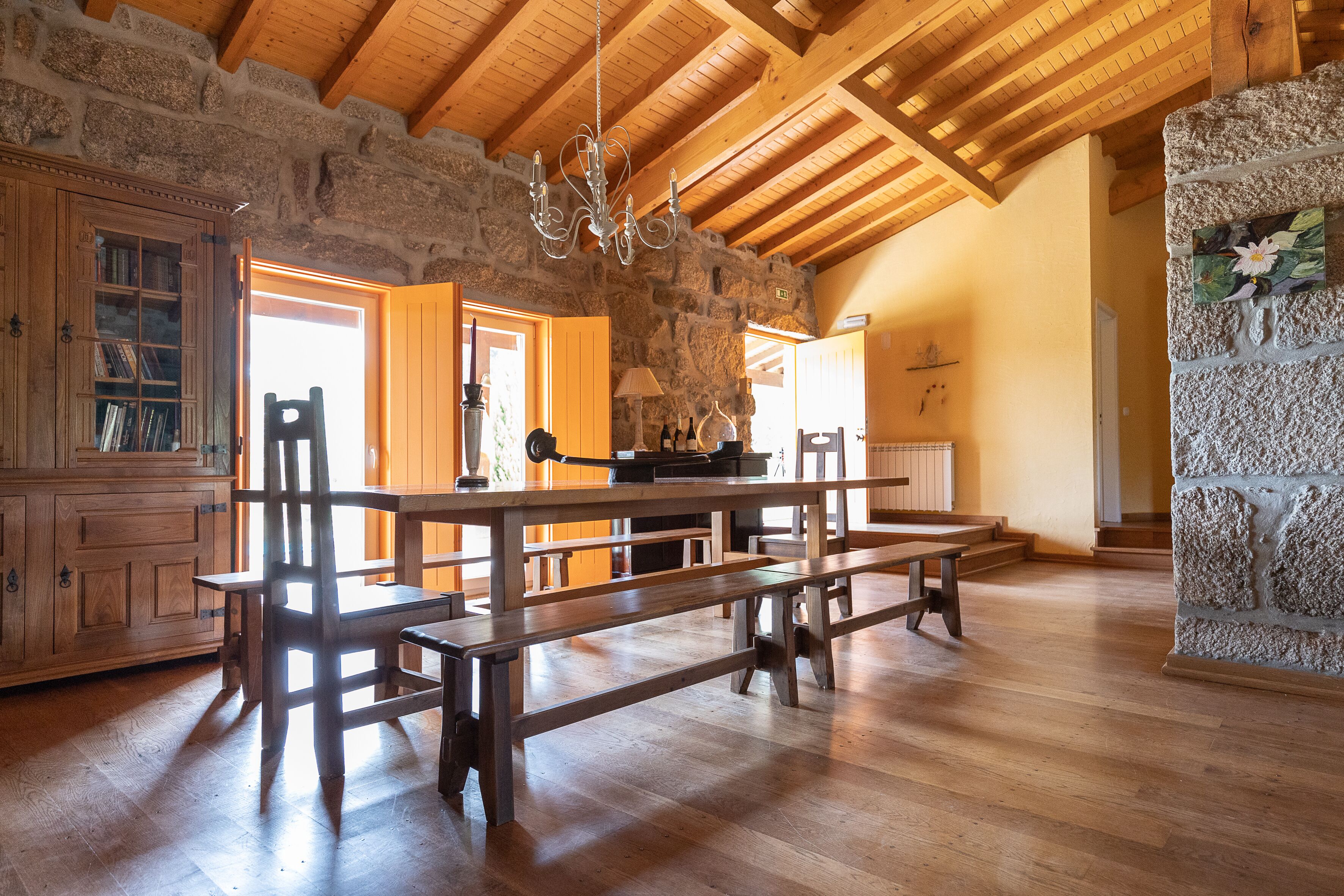 A rustic interior with wooden benches, a stone wall, and a chandelier.
