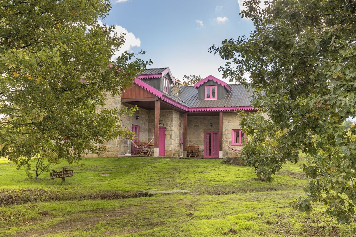 A stone building with pink accents, a covered porch, and a grassy area in front.